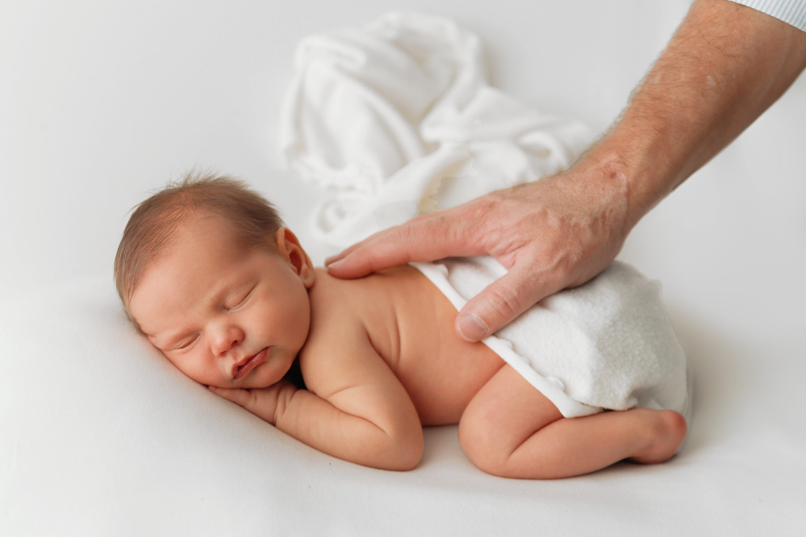 baby boy on all white with dads hand on his back i