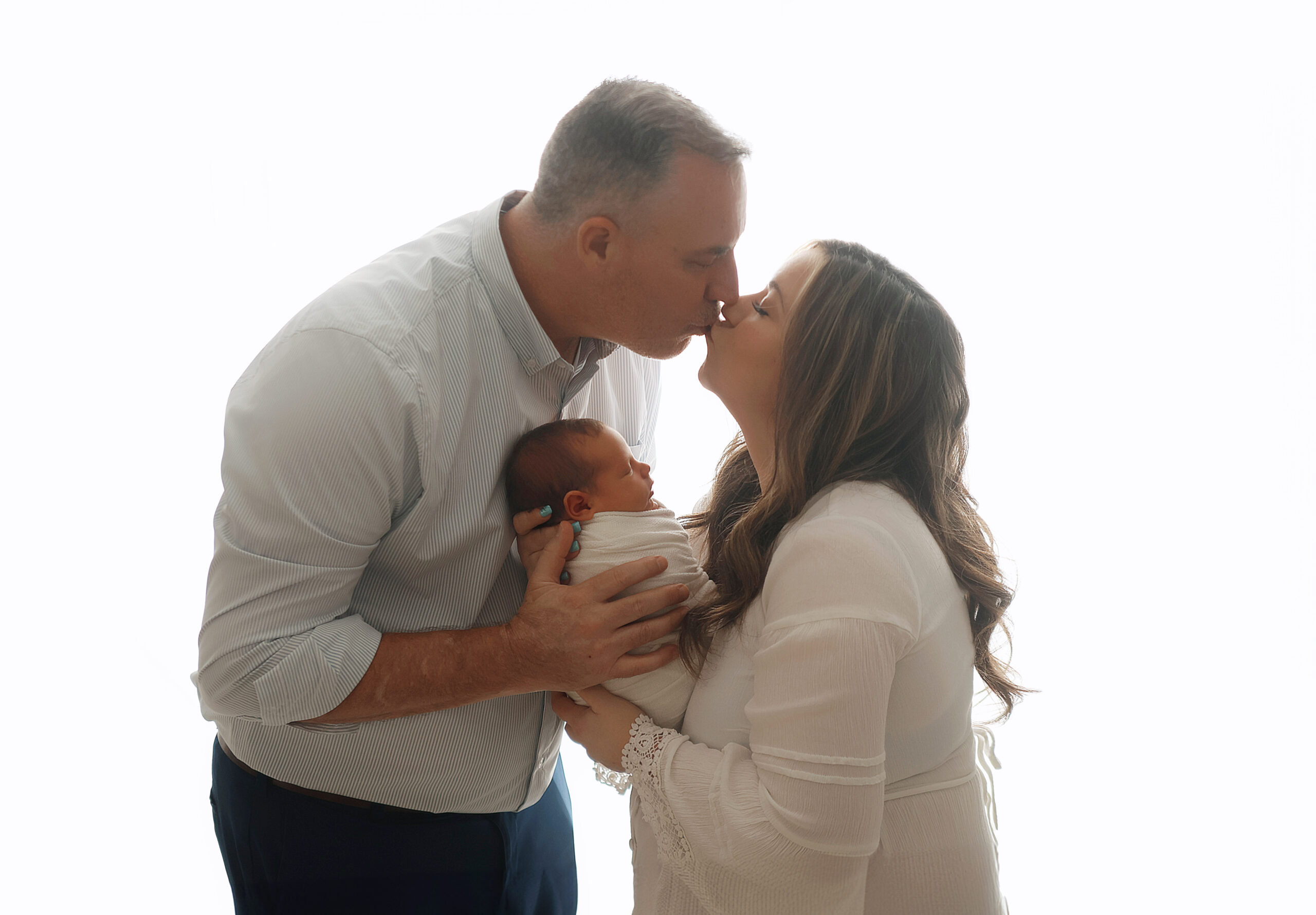 husband and wife kissing over baby boy in Claremore newborn photography studio