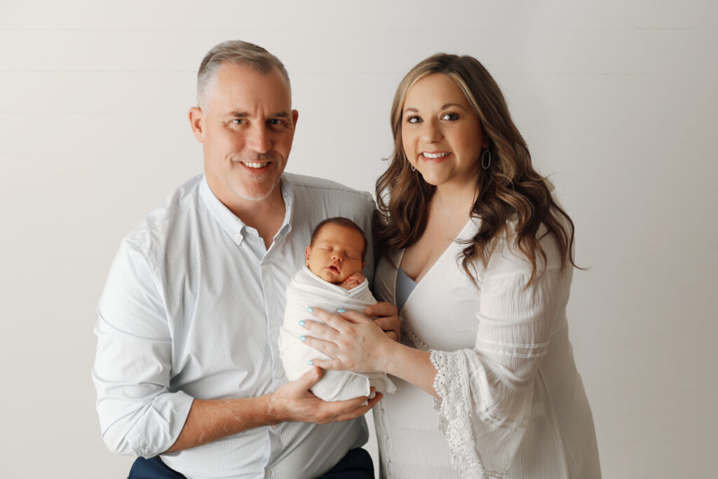 husband and wife smiling with their surprise baby boy in Claremore newborn photography studio