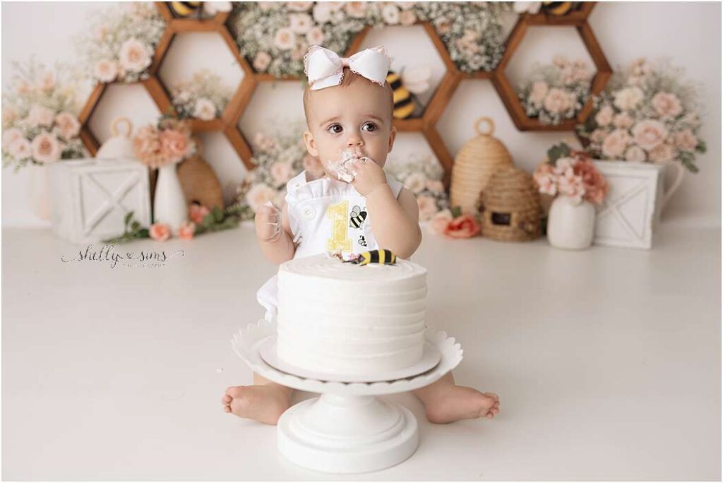 Baby celebrating first birthday with a bee-themed cake smash surrounded by flowers and honeycomb décor — photographed by Shelly Sims Photography in Owasso.