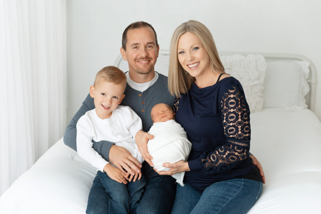 of four smiling together with their newborn wrapped in white, captured during a newborn photography session in Owasso by Shelly Sims Photography.
